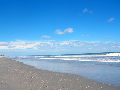 Bright blue sky, breaking waves, and a long stretch of beach in Corolla, North Carolina